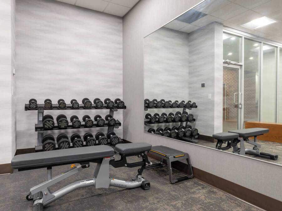 Uma academia com equipamentos de musculação, bancos e um espelho grande.