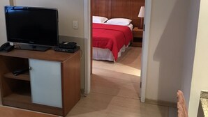 A hotel room with a bed, a desk with a television, and a small cabinet.