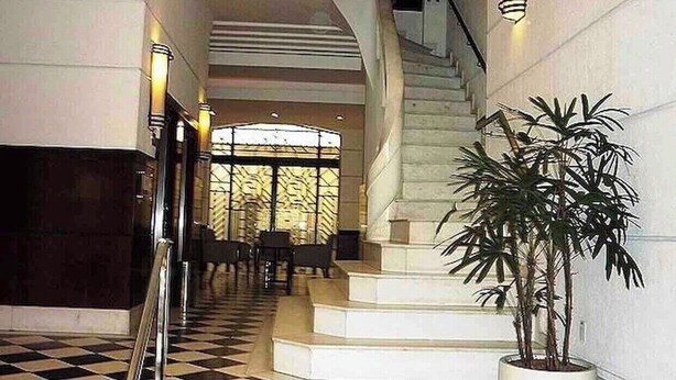 A lobby with a checkered floor, a staircase, and a large potted plant.