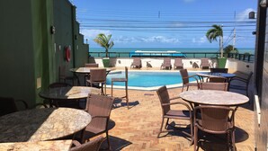Un espace piscine aménagé sur le toit, avec des meubles en osier et une vue sur l’océan.