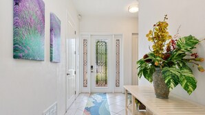 A hallway with a tiled floor, a door with a glass panel, and a vase with flowers on a table. - Lux Ocean View 4x4 for the Holidays! (Holmes Beach)