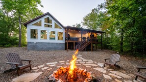 Une maison moderne dotée d’un foyer en pierre, d’une terrasse en bois et de deux fauteuils Adirondack.