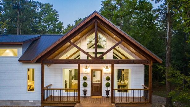 Une cabane en bois avec un toit à pignon, de grandes fenêtres et une véranda dotée de balustrades.