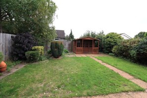A backyard with a wooden shed, a lawn, and a variety of plants.