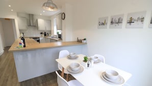 Una cocina moderna con gabinetes blancos, una isla de madera y un comedor con sillas y platos blancos.