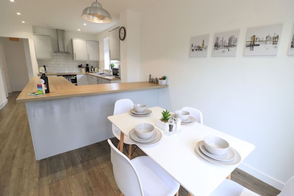 Une cuisine moderne avec des meubles blancs, un îlot central en bois et un coin repas avec des chaises et des assiettes blanches.