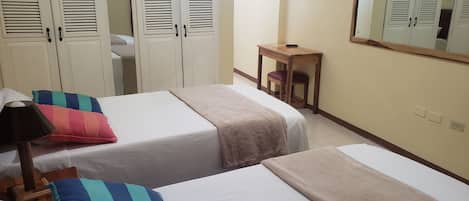 A hotel room with two beds, a wooden desk, a chair, a lamp, and a mirror on the wall.