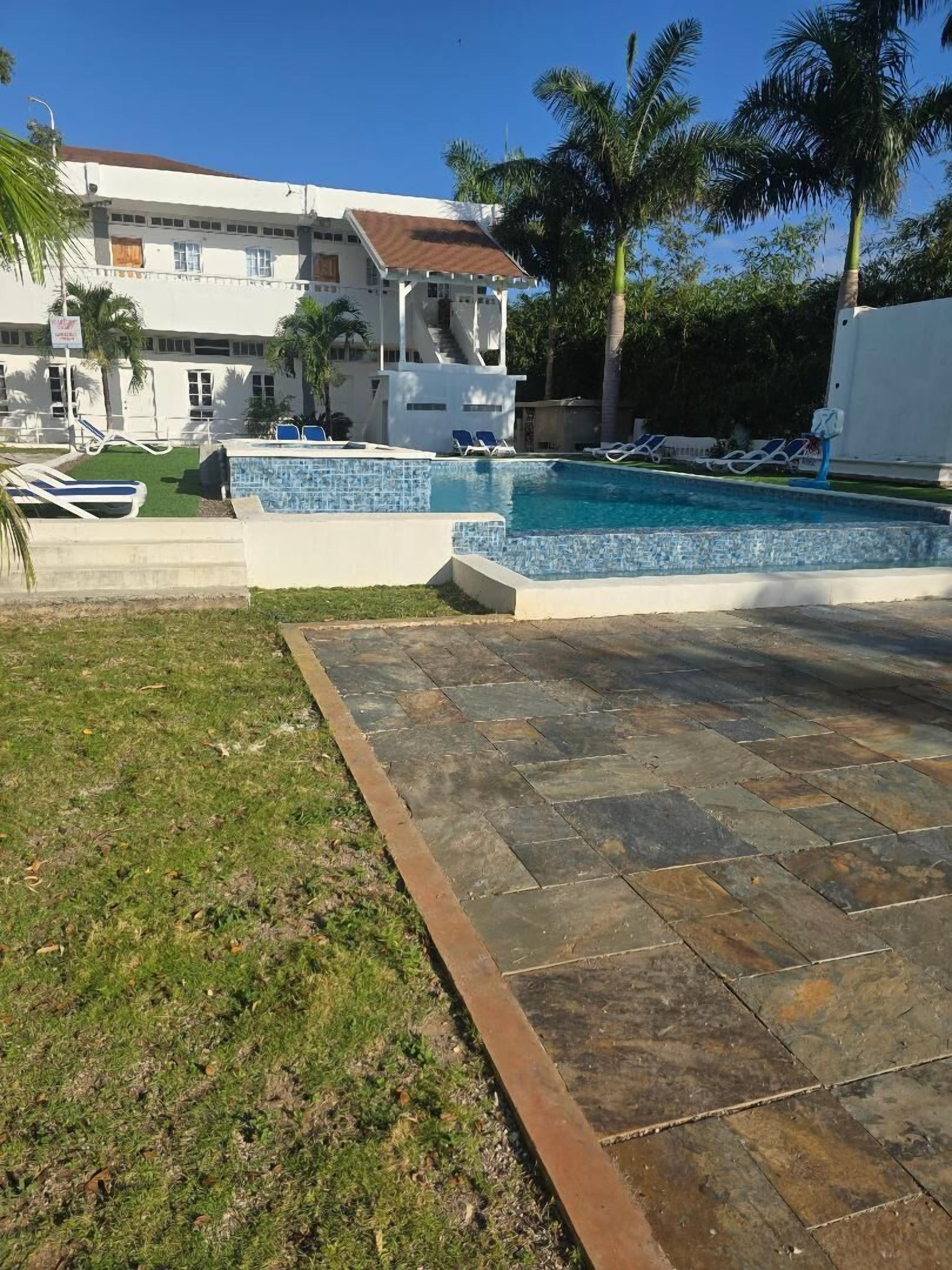 A swimming pool with a tiled deck, lounge chairs, and palm trees.
