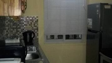 Una cocina con un lavamanos, una ventana con persianas, un refrigerador y armarios de madera.