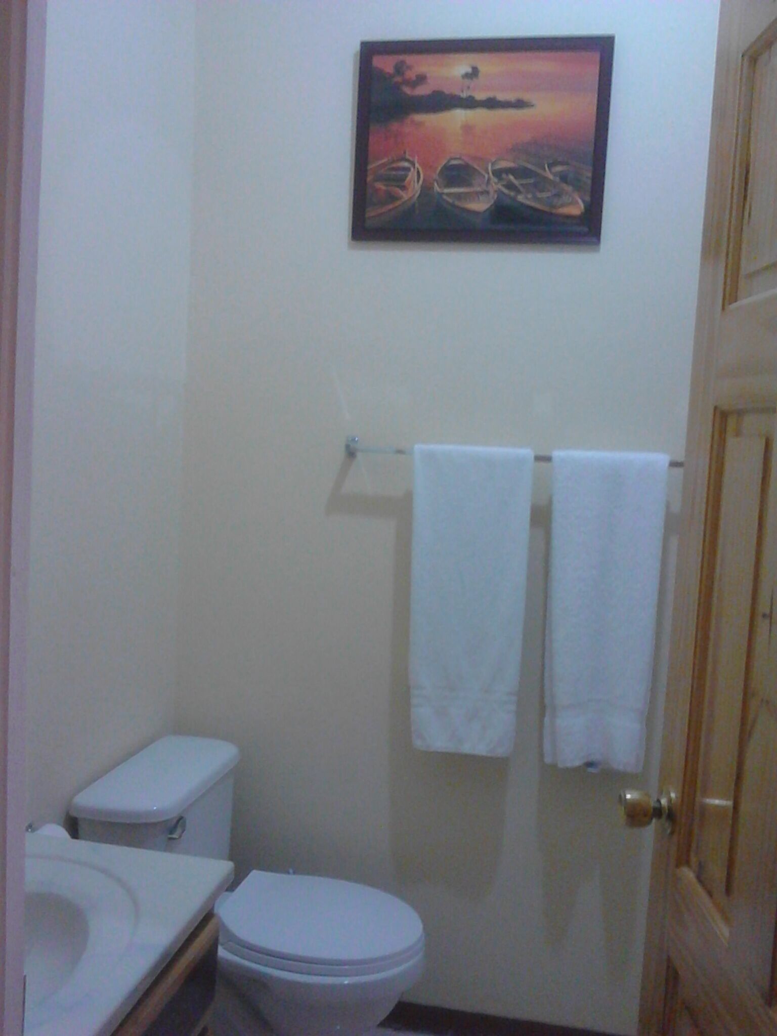 A small bathroom with a toilet, sink, and a painting of boats on the wall.