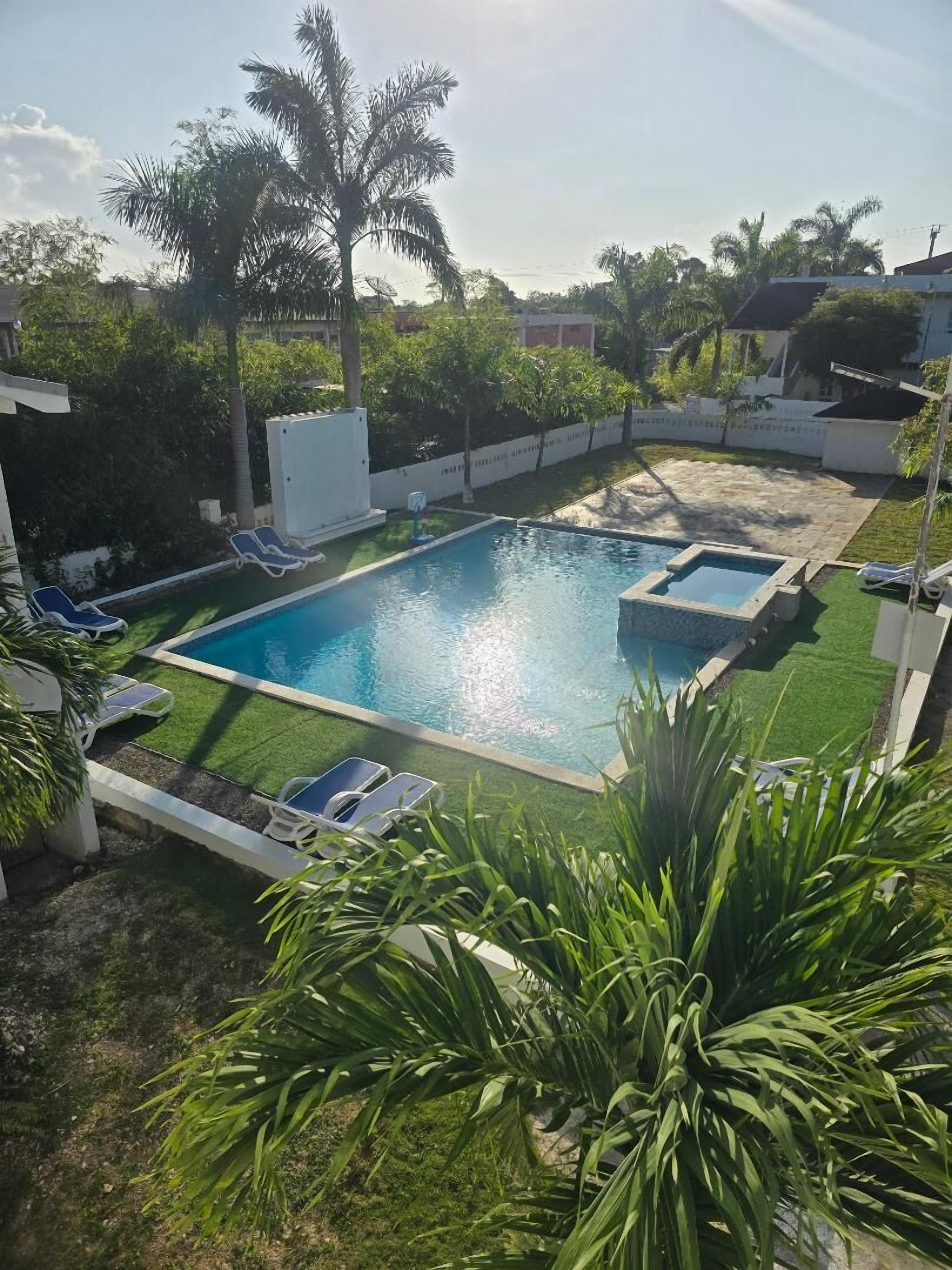 Piscina retangular com duas piscinas menores, rodeada por um gramado bem cuidado e palmeiras.