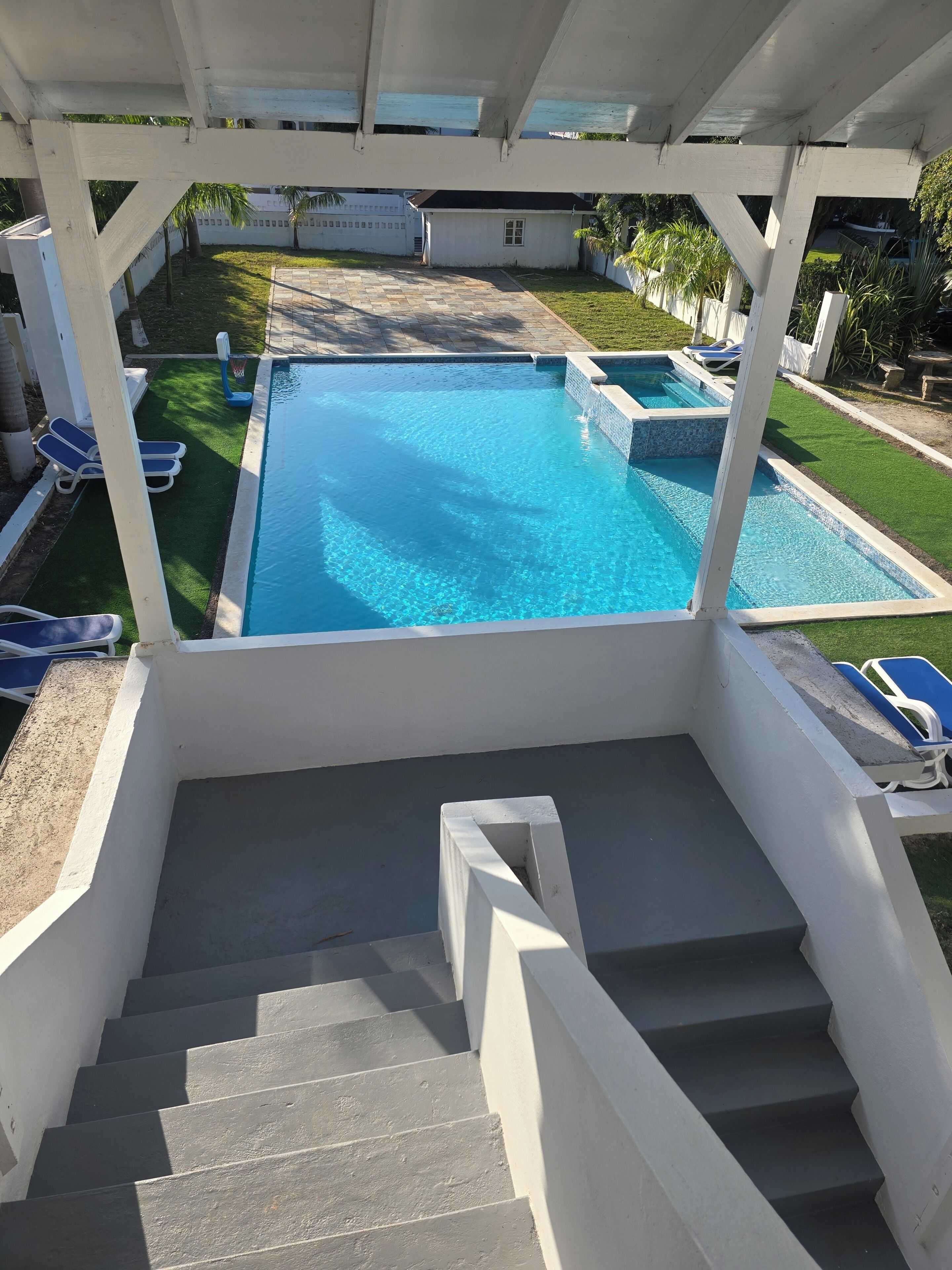 A swimming pool with a clear blue water, surrounded by a white structure, and a set of stairs leading down to the pool area.