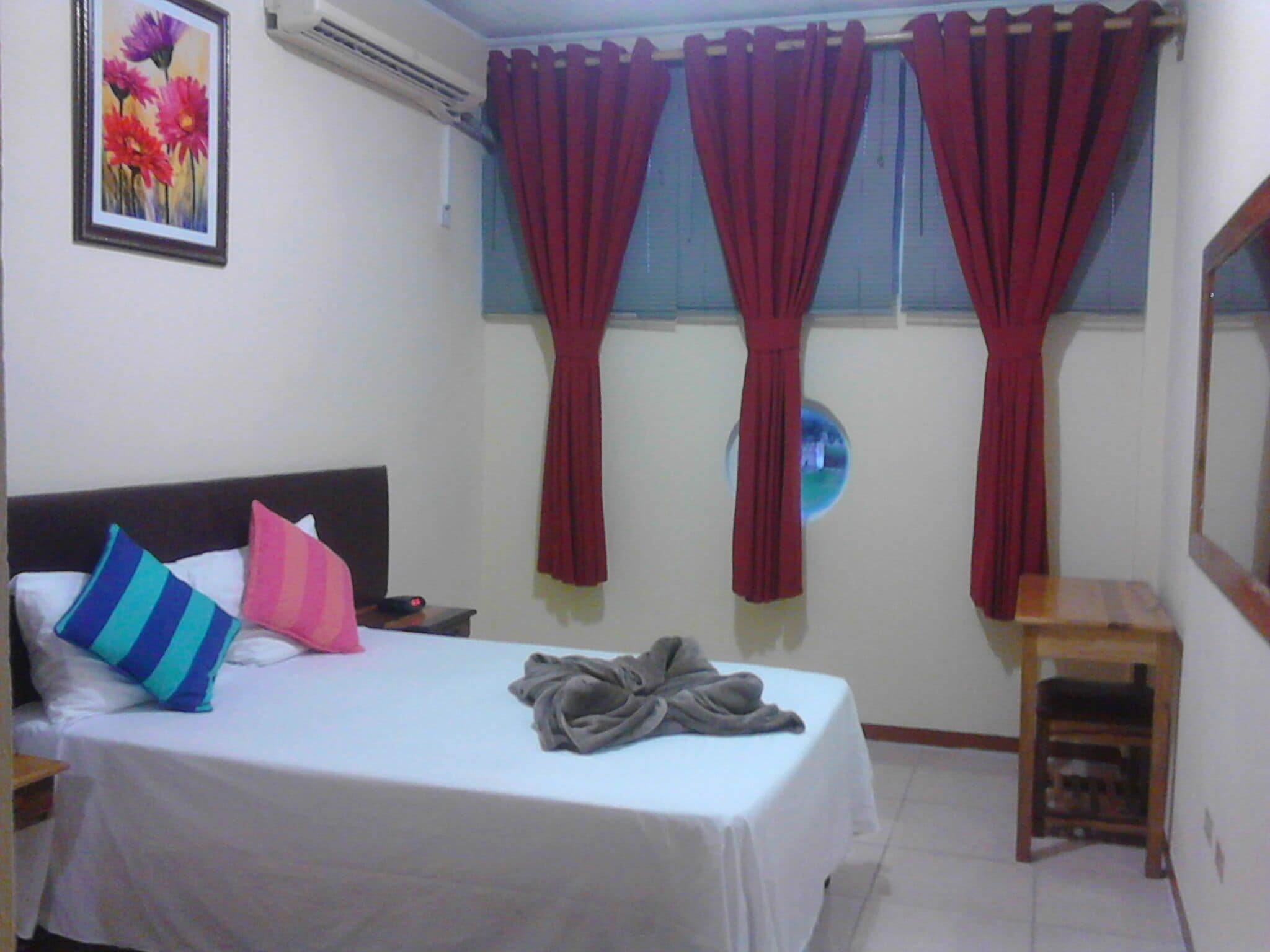 Un dormitorio con cama, almohadas, una mesita de noche, un taburete de madera y un aire acondicionado de pared.