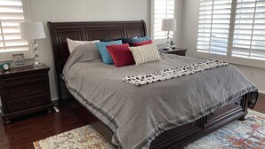 Een keurig opgemaakt slaapkamer met een groot bed, twee nachtkastjes en een raam met jaloezieën.