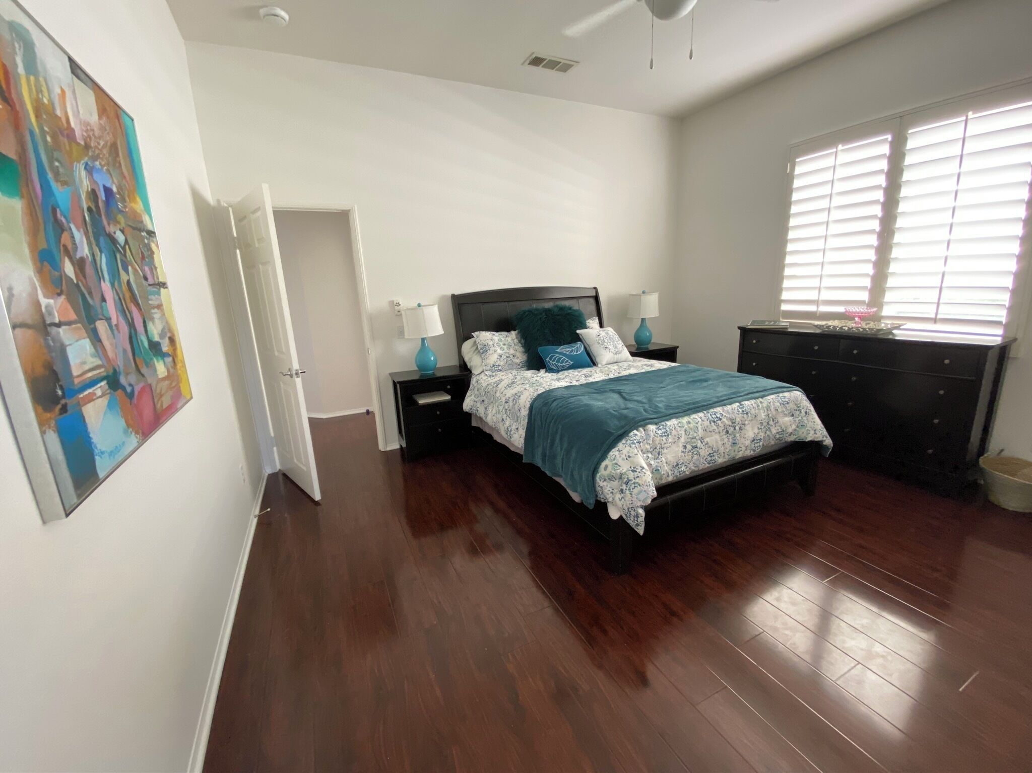 Une chambre à coucher comprenant un lit, des tables de chevet, une commode, une fenêtre avec des stores et une porte donnant sur une autre pièce.