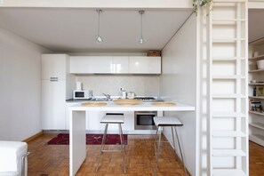 Una cocina moderna con armarios blancos, un microondas, una estufa y dos taburetes de bar.
