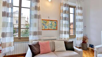 Un salon avec un canapé, un radiateur, une fenêtre avec des rideaux et un tableau accroché au mur.