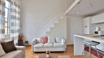 Un salon moderne avec un canapé, une table basse et un escalier menant à un espace cuisine.
