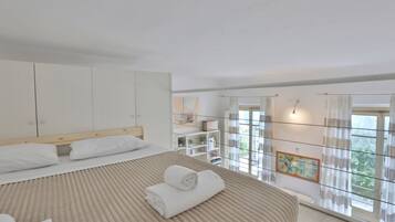 Une chambre avec un grand lit, une armoire, un bureau et une vue sur la verdure par la fenêtre.
