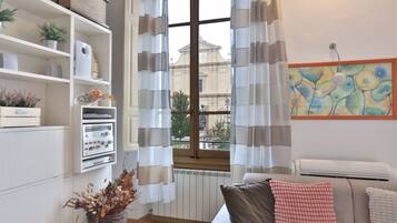 Een woonkamer met een bank, een radiator, een raam met gordijnen en een aan de muur hangend kunstwerk.