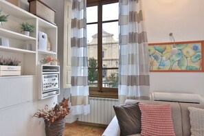 Una sala de estar con sofá, un radiador, una ventana con cortinas y una obra de arte colgada en la pared.