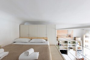 A modern bedroom with a large bed, a wooden headboard, a white wardrobe, and a built-in shelving unit with books and decorative items. - GuestHost - Bright and functional 50sqm studio apartment that can accommodate up to 3 people. Located on the first floor, with elevator (not suitable for disabled), of a building overlooking Piazza San Marco and the homonymous Basilica, the apartment is  (Firenze)