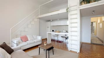 Een moderne woonkamer met een witte bank, een salontafel en een trap die leidt naar een keukenhoek.