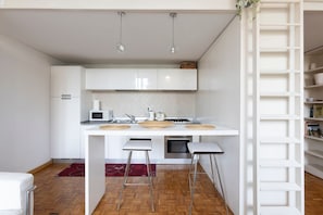 A modern kitchen with white cabinetry, a microwave, a stove, and two bar stools. - GuestHost - Bright and functional 50sqm studio apartment that can accommodate up to 3 people. Located on the first floor, with elevator (not suitable for disabled), of a building overlooking Piazza San Marco and the homonymous Basilica, the apartment is  (Firenze)