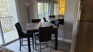 Une cuisine moderne avec une table et des chaises, un réfrigérateur et une grande fenêtre donnant sur l’extérieur.