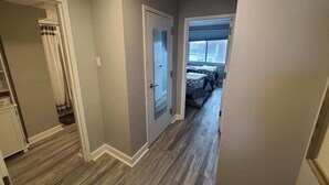 Un couloir étroit avec une porte donnant sur une chambre à coucher, où se trouvent un lit et une fenêtre.