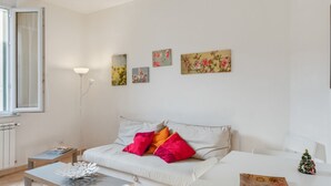 Ein modernes Wohnzimmer mit einer Couch, einem Couchtisch und einem kleinen Tisch mit einem dekorativen Gegenstand. An den Wänden befinden sich Bilder, und es gibt eine Stehlampe.