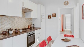 Eine moderne Küche mit weißen Schränken, einer Ziegelrückwand und einem Essbereich mit einem weißen Tisch und roten Stühlen.
