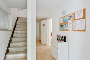 A staircase leading to a room, a bulletin board with notices, and a small white cabinet with books and a mug.