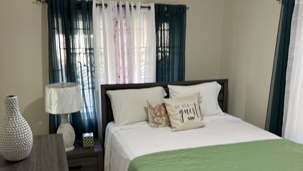 Un dormitorio con cama, mesita de noche, lámpara y cortinas.