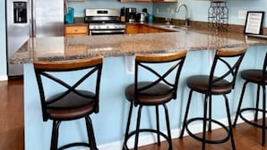 A modern kitchen with wooden cabinets, stainless steel appliances, a granite countertop, and three bar stools. - Huge 4 Bedroom, Beach Block Condo with Pool and 3 Parking Spaces.   (North Wildwood)