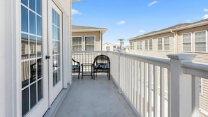 A balcony with a white railing, a glass door, and two wicker chairs. - Huge 4 Bedroom, Beach Block Condo with Pool and 3 Parking Spaces.   (North Wildwood)