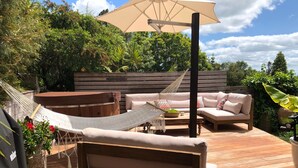 Eine Holzterrasse mit einer Hängematte, einer gepolsterten Bank und einer Couch unter einem großen Sonnenschirm.