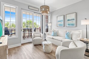 A modern living room with a white sofa, armchairs, a round ottoman, a floor lamp, and a large window with a view of palm trees. - Luxurious 3 BR Condo overlooking 30A nestled between Rosemary & Alys Beach (Rosemary Beach)