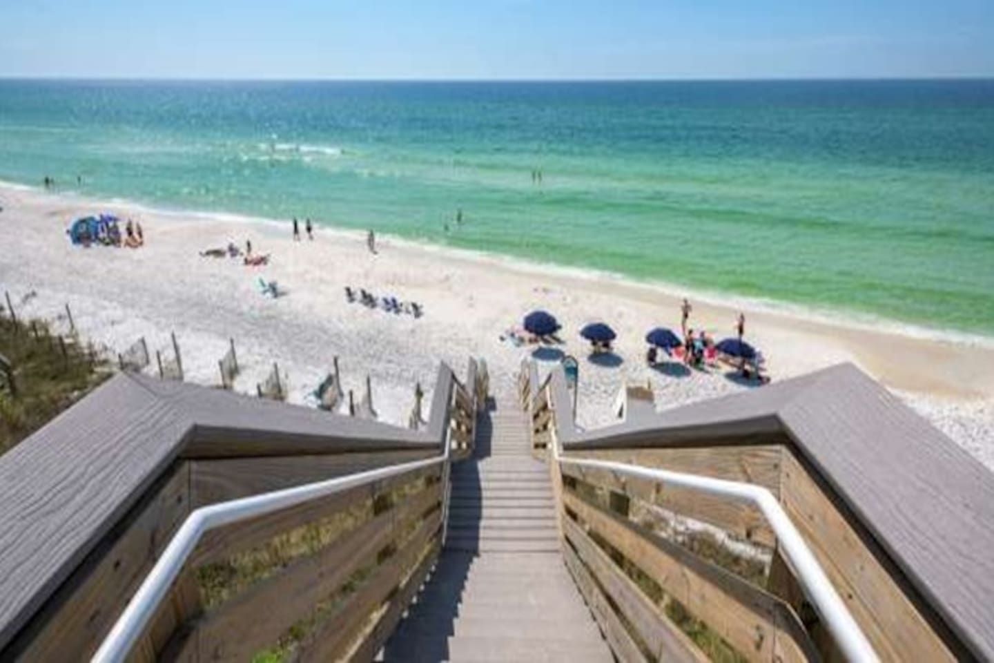 A wooden staircase leading to a beach with umbrellas and people.