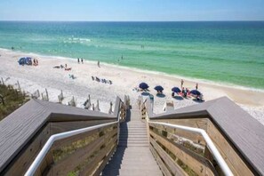 A wooden staircase leading to a beach with umbrellas and people.