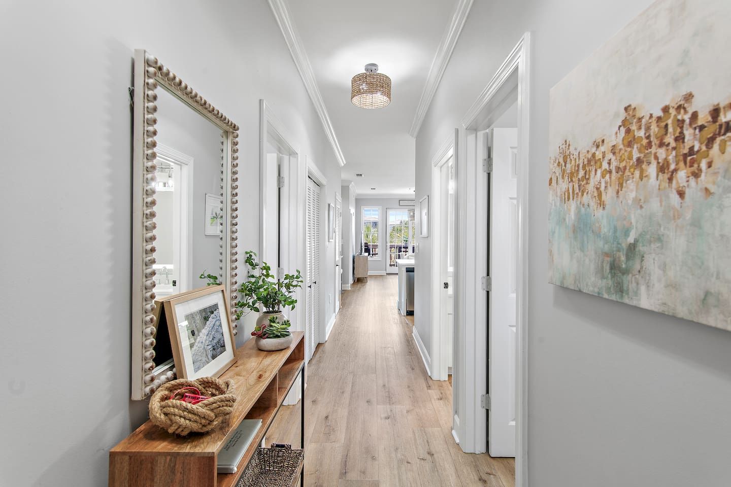 A hallway with a wooden bench, a mirror with lights, a plant, and a painting on the wall.