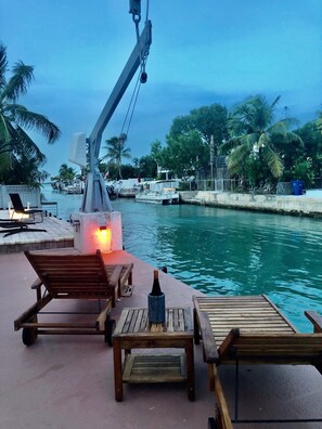 A waterfront deck with wooden lounge chairs and tables, a docked boat, and a crane structure. - Fisherman's Paradise on the Water (Key West)