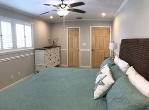 Ein Schlafzimmer mit Bett, Schminktisch, Deckenventilator und zwei Türen.