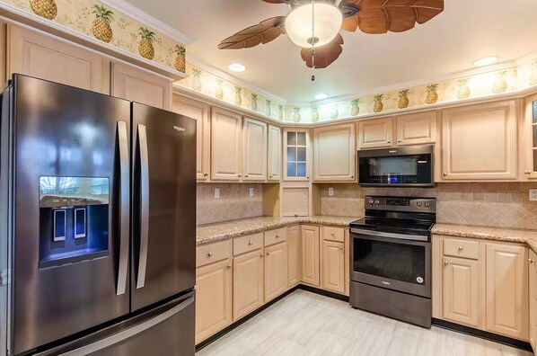 A kitchen with light wood cabinets, stainless steel appliances, and a pineapple-themed wallpaper. - Fisherman's Paradise on the Water (Key West)