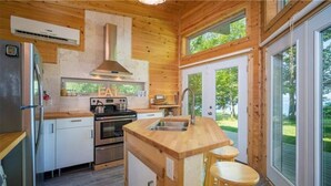 A modern kitchen with wooden walls, a stainless steel refrigerator, a double oven, and a wooden island with stools.