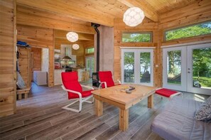 A wooden cabin interior with a dining table, red chairs, a sofa, and large windows. - The Sunset Hideaway in Portland, NY (Brocton)