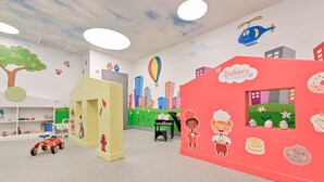 Un salón de juegos para niños con un mural con temática de panadería, un coche de juguete y una pintura mural de un paisaje urbano.