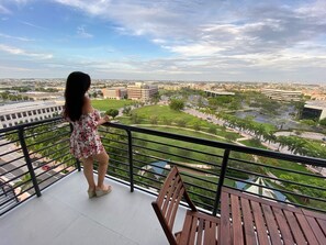 Een balkon met uitzicht op een stadsgezicht, een vrouw staand, en een houten tafel.