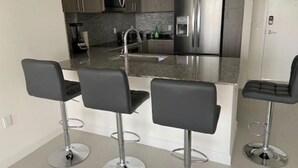 Una cocina moderna con electrodomésticos de acero inoxidable, encimera de granito y tres taburetes negros.