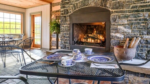 A cozy outdoor seating area with a stone fireplace, metal tables, and blue and white patterned tableware. - Bed & Breakfast in a 1795 Log Cabin on working farm, George Washington, Sr Suite (Swoope)